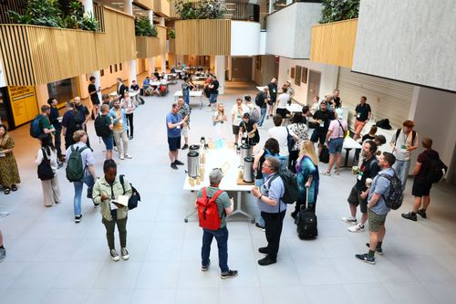 Top down view of an atrium, modern light and wood panelled, attendees mingle with coffee.