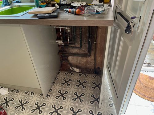 Exposed gas and water pipes below a kitchen worktop.