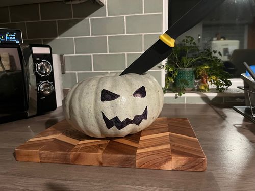 A pumpkin with Halloween-style face drew on with marker. It's friendly, it's menacing, it has a kitchen knife in its head.