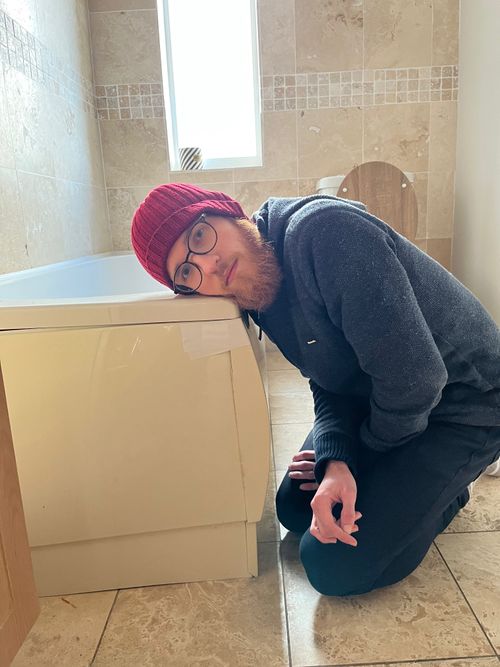 Me knelt by a bath, my head laid on its corner. White tape holds the side panels of the bath together. Also of note is my favourite red hat and ginger beard, which some – definitely not myself – may say is magnificat (I wonder if anyone finds this description?)