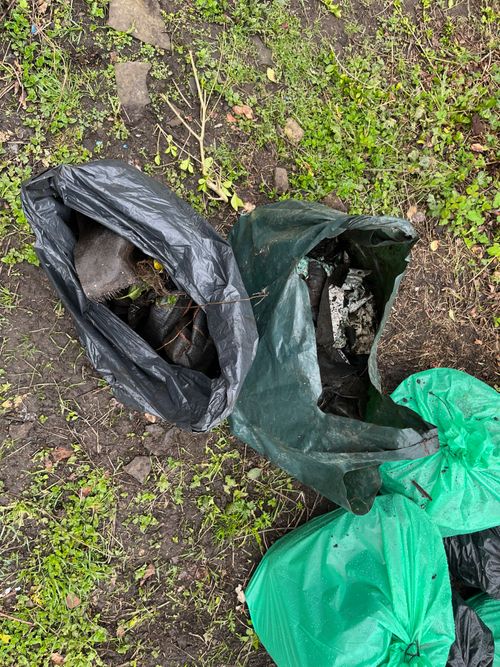Open bin-liner sized bags showing rubbish collected from the plot. Includes lots of plastic, including disintegrating bags of compost, weed suppressing membrane – covered with mud and entangled with nature.