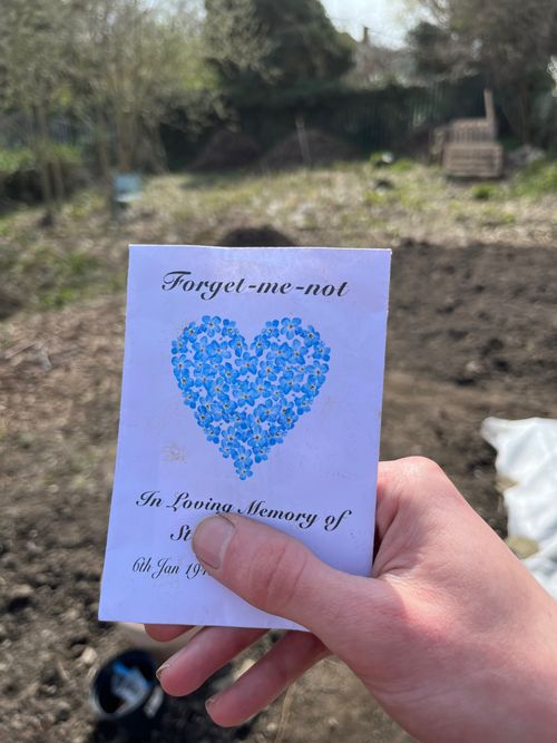 Holding a paper packet of seeds to the camera. Personal details obscured, it reads: forget-me-not. In loving memory of St... 6th Jan 19...