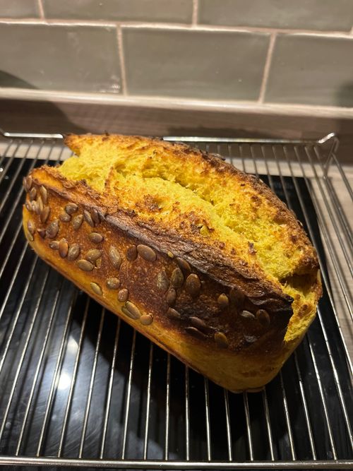 A tin loaf of bread, with an unusual but attractive orange hue and pumpkin seeds.