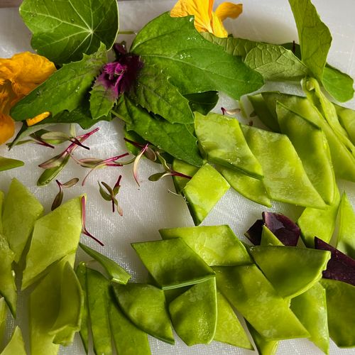 Peas, flowers, and editable foliage chopped up on a chopping board.
